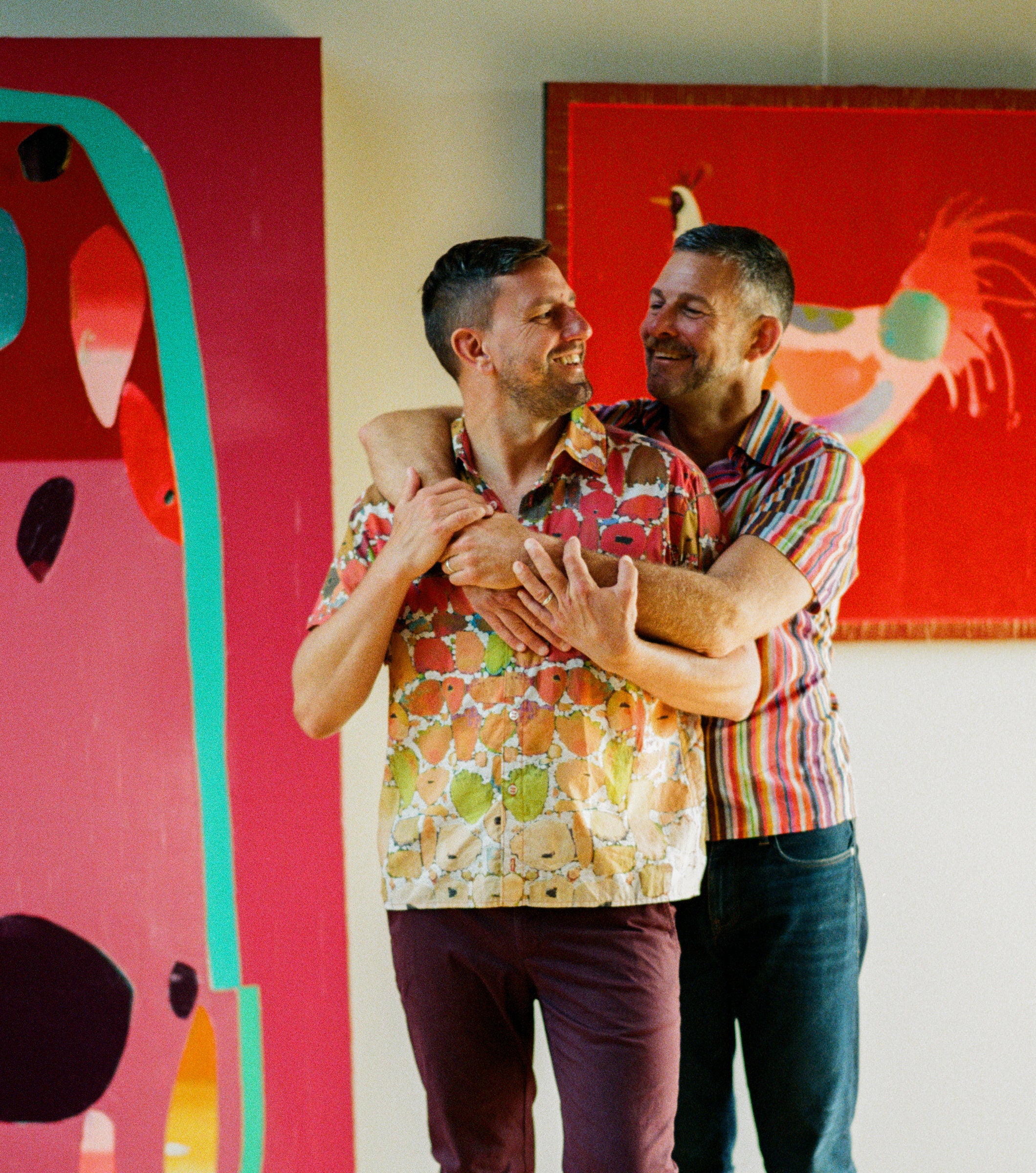 Two people embracing in a room with colorful abstract art on the walls. Artist Trevor Mikula and his partner.