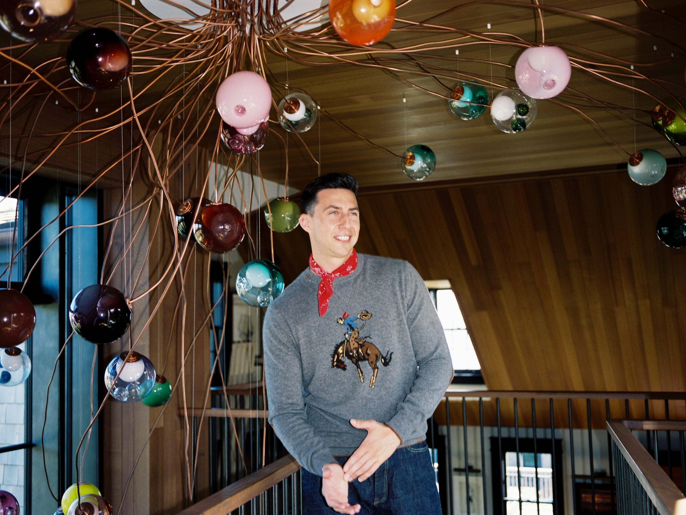 Man wearing a cashmere sweater with a cowboy design in a room with colorful ceiling lights.