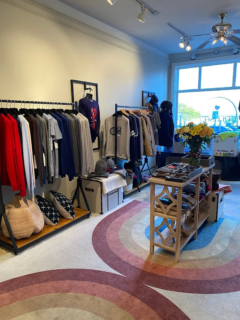Daniel Hammond / Plush Provincetown store interior with racks of clothes and a colorful carpet.