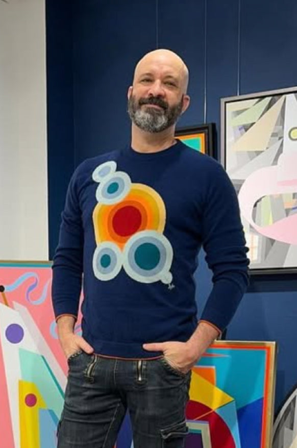 Man wearing a navy blue Daniel Hammond iconic cashmere sweater with a colorful abstract design in an art gallery.