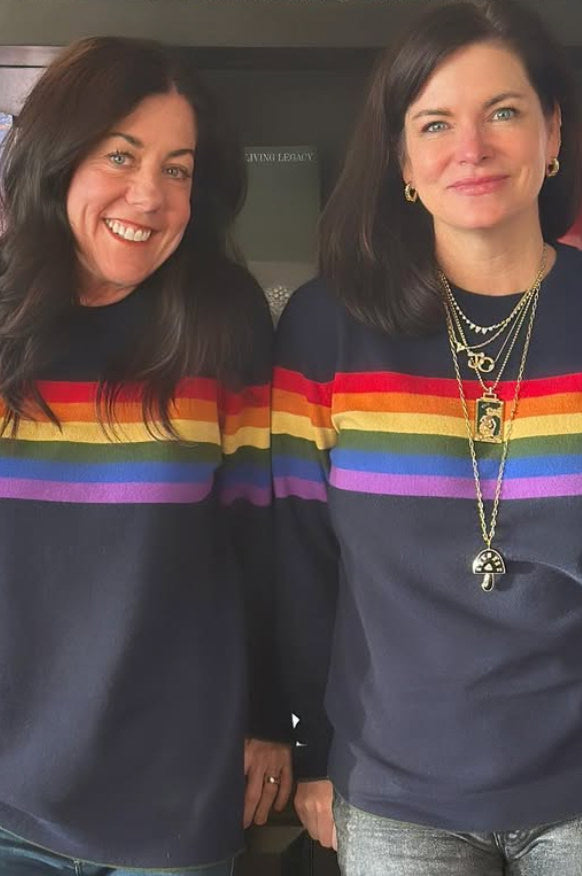 Two women wearing rainbow striped Daniel Hammond cashmere sweaters standing next to each other.