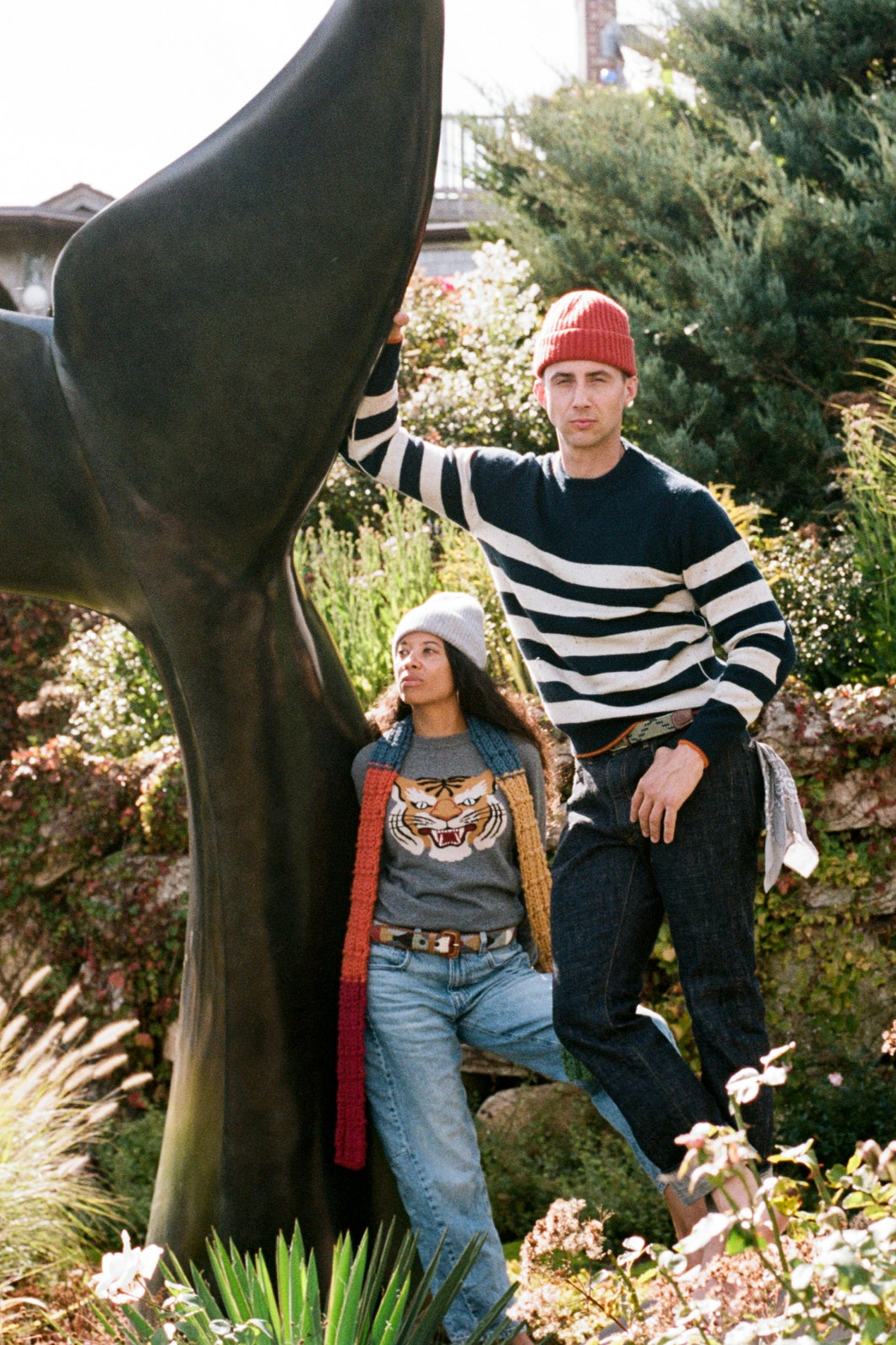 Two people wearing Daniel Hammond cashmere, standing next to a large whale tail sculpture in a garden setting in Provincetown, Cape Cod, New England, USA.