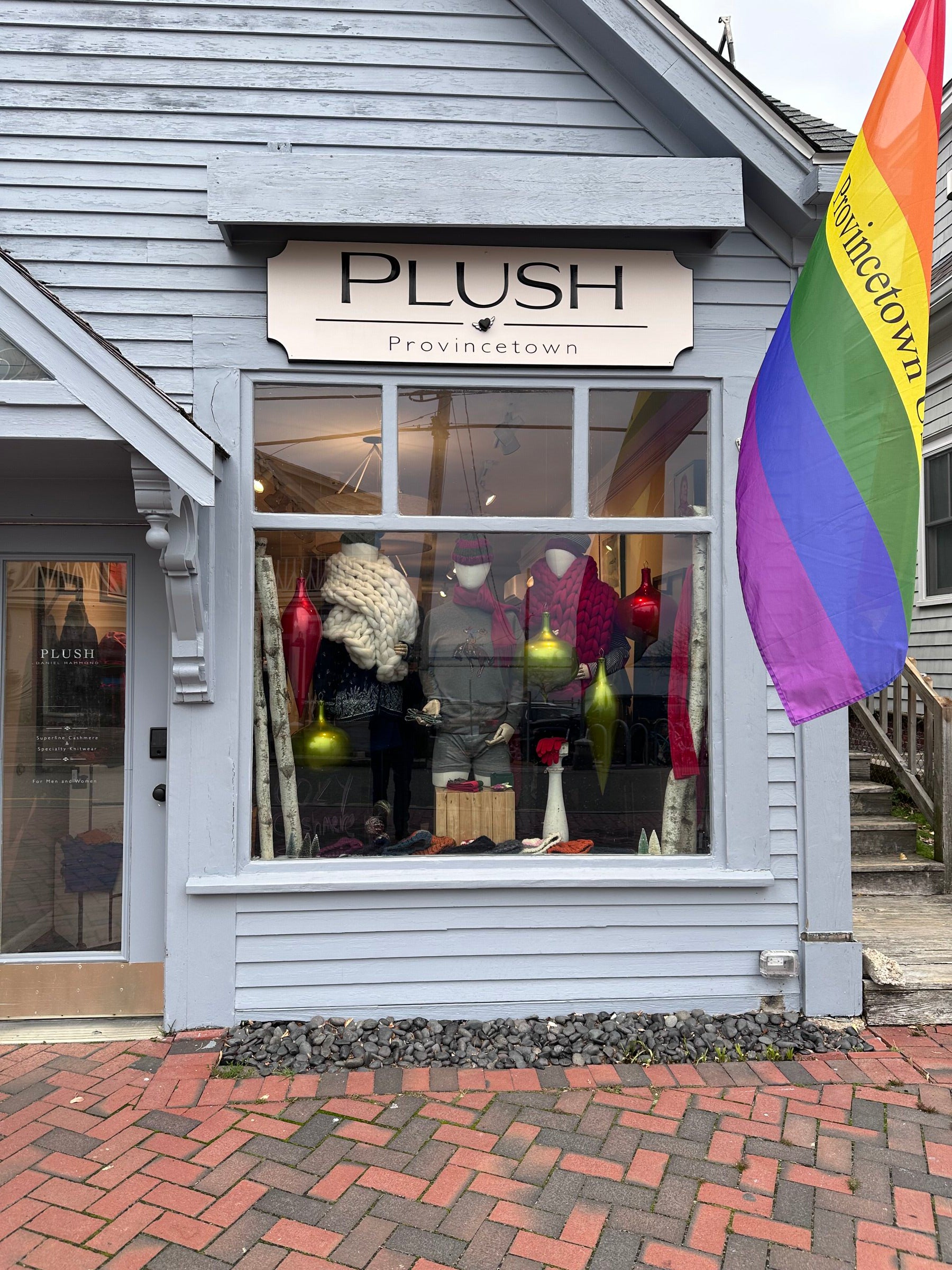 Daniel Hammond storefront in Provincetown, Cape Cod, New England, USA with rainbow flag above and brick sidewalk in Ptown's Historic District.