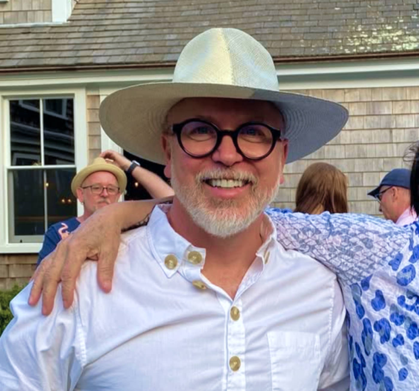 Daniel Hammond wearing a white hat and glasses with a beard, standing outdoors with people around.