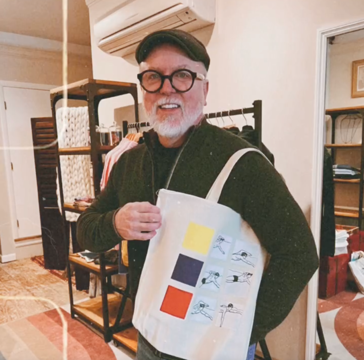 Man holding a tote bag with colorful designs in a room with shelves and furniture.